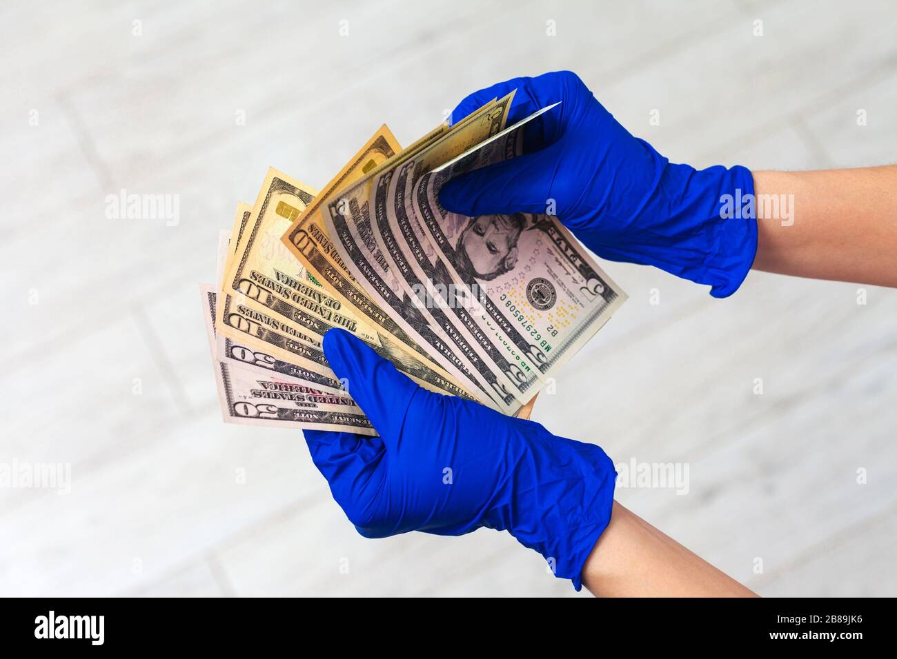 Mani in guanti per uso medico in possesso di un pacchetto di dollari. Il concetto di infezione su soldi, soldi sporchi, medicina paid, tasse di trattamento, tangenti, chirurgia illegale. Foto Stock