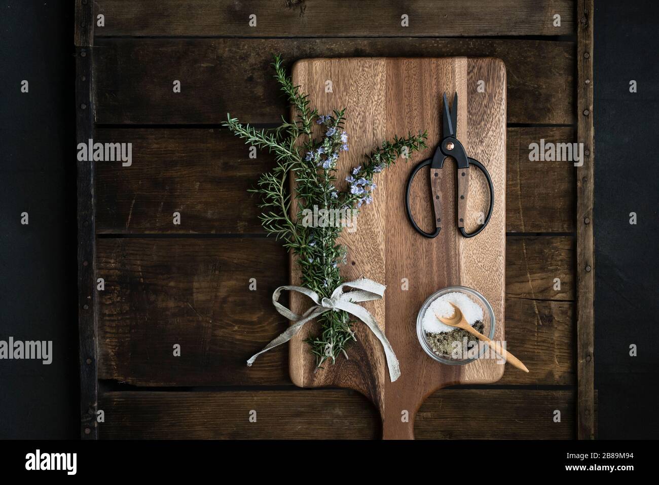 fascio di rosmarino fresco, sale grosso, forbici su tagliere Foto Stock