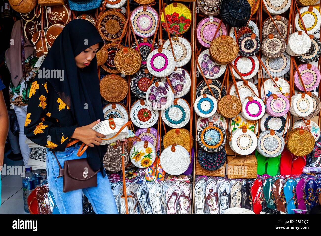 Una giovane donna dorsa le borse/borse che sono in vendita, il mercato d'arte di Sukawati, Gianyar, Bali, Indonesia. Foto Stock