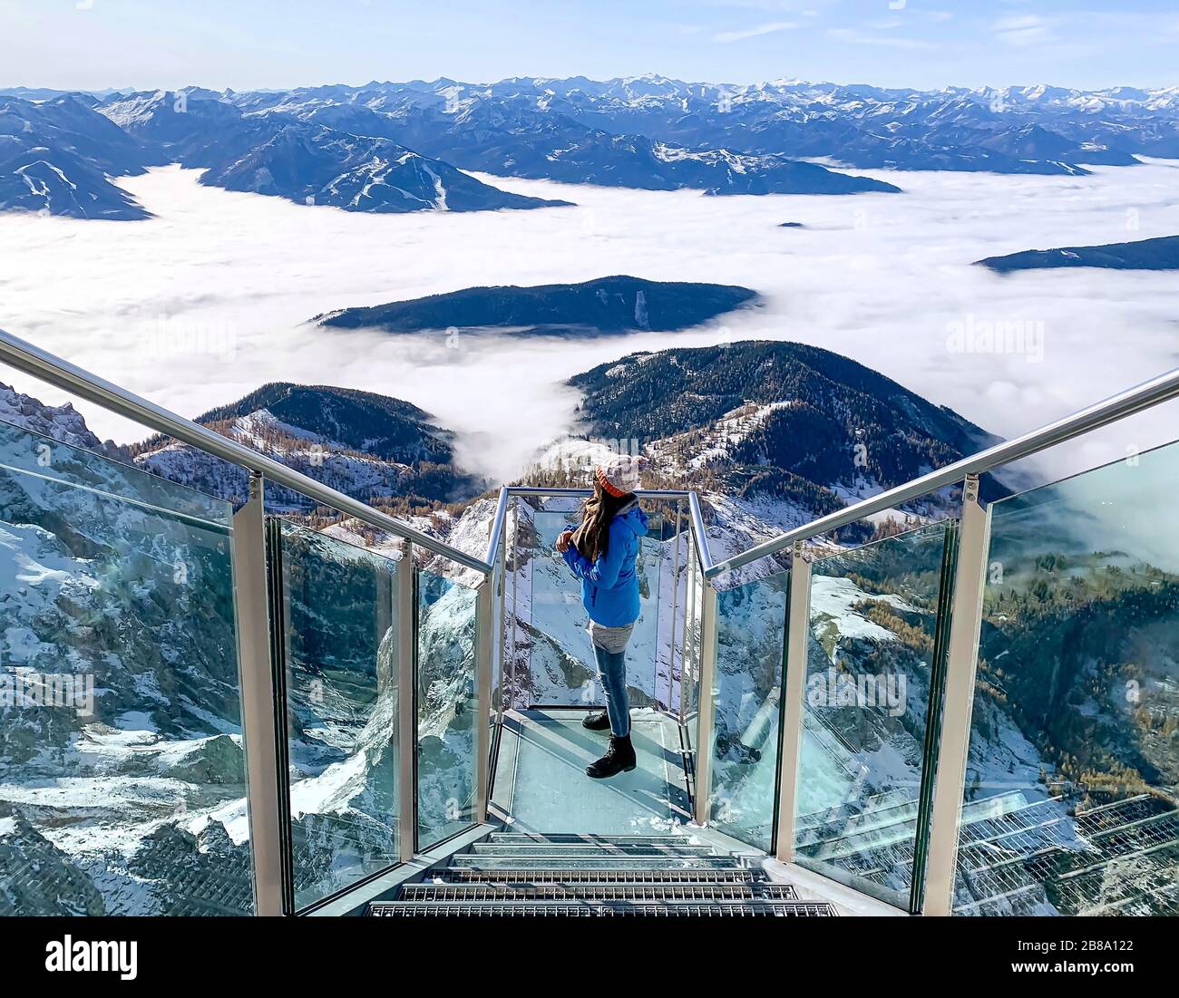 Donna in piedi sul vetro del passerella a Dachstein, godendo di vista delle montagne innevate in Austria durante le vacanze invernali Foto Stock