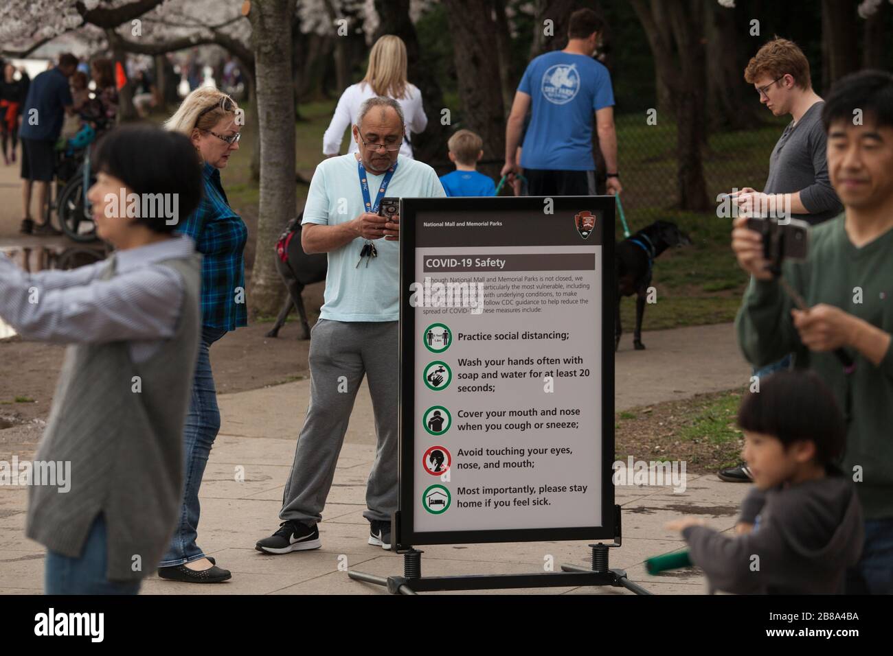 La gente circonda un avviso di sicurezza di COVID19 vicino ai blossoms del Cherry al bacino del Tidal a Washington, D.C., 20 marzo 2020, meno gente che normale. Foto Stock