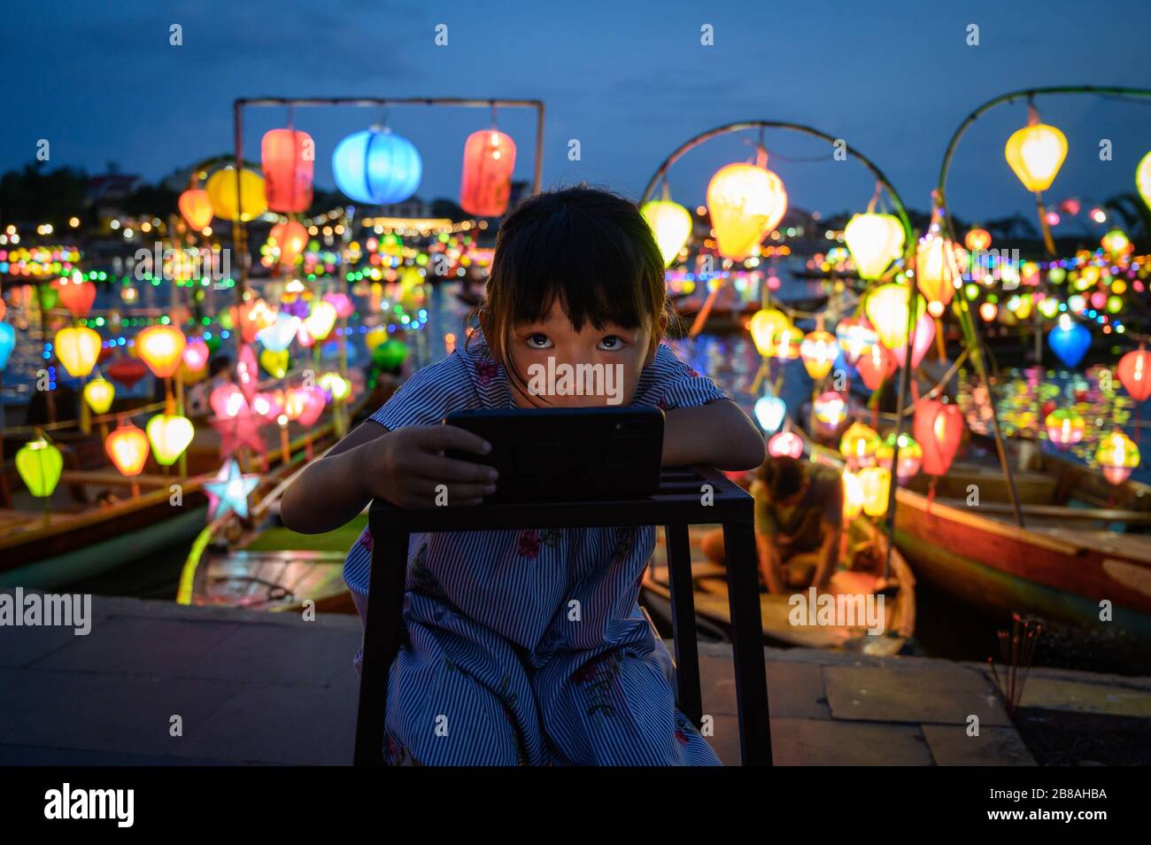 Giovane ragazza al telefono contro le lanterne della barca a Hoi An, Vietnam Foto Stock