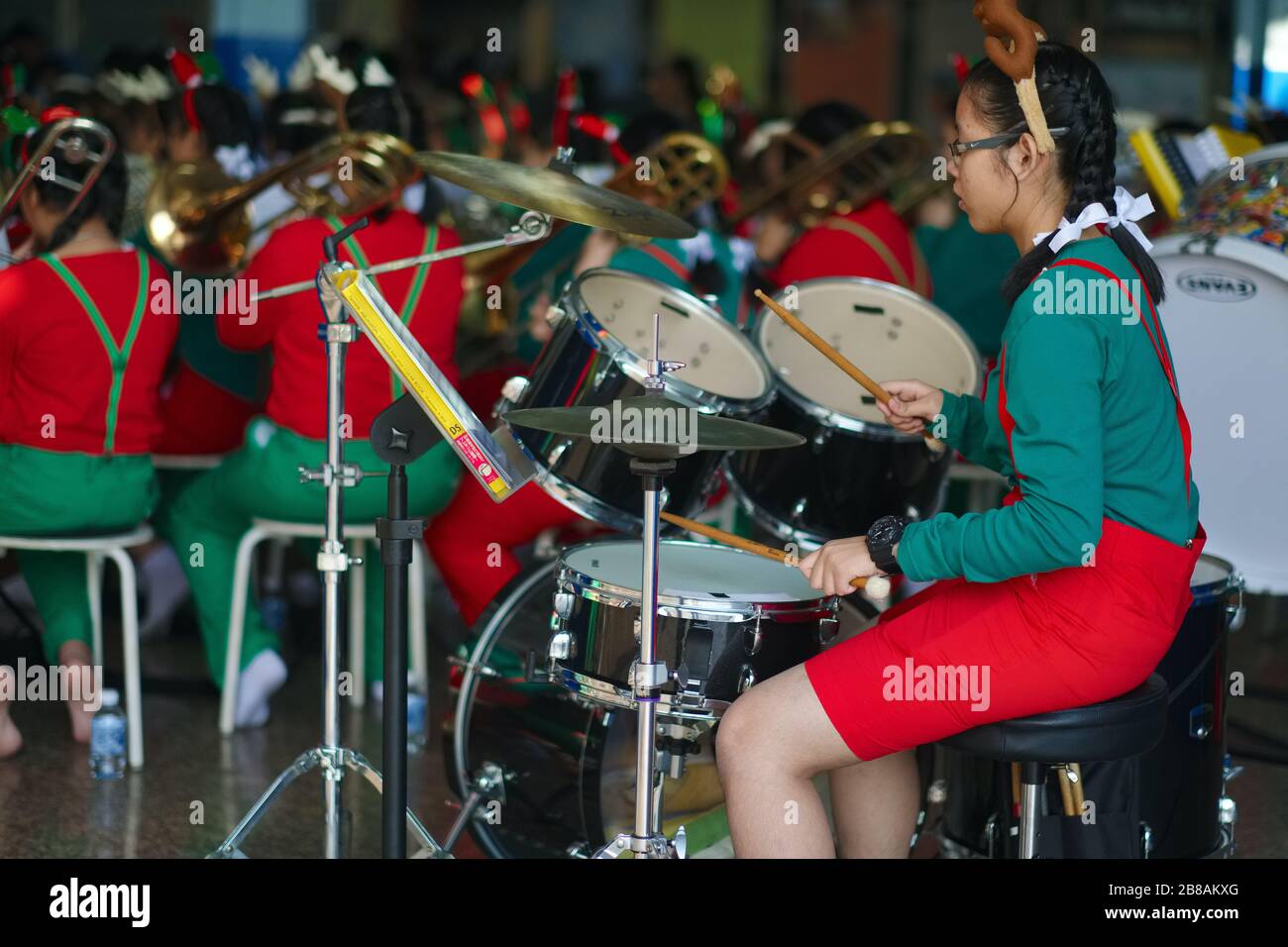 Una ragazza batterista, una allieva in una scuola accanto Santa Cruz Chiesa a Thonburi, Bangkok, Thailandia, con la sua band di scuola che prova per un programma di Natale Foto Stock