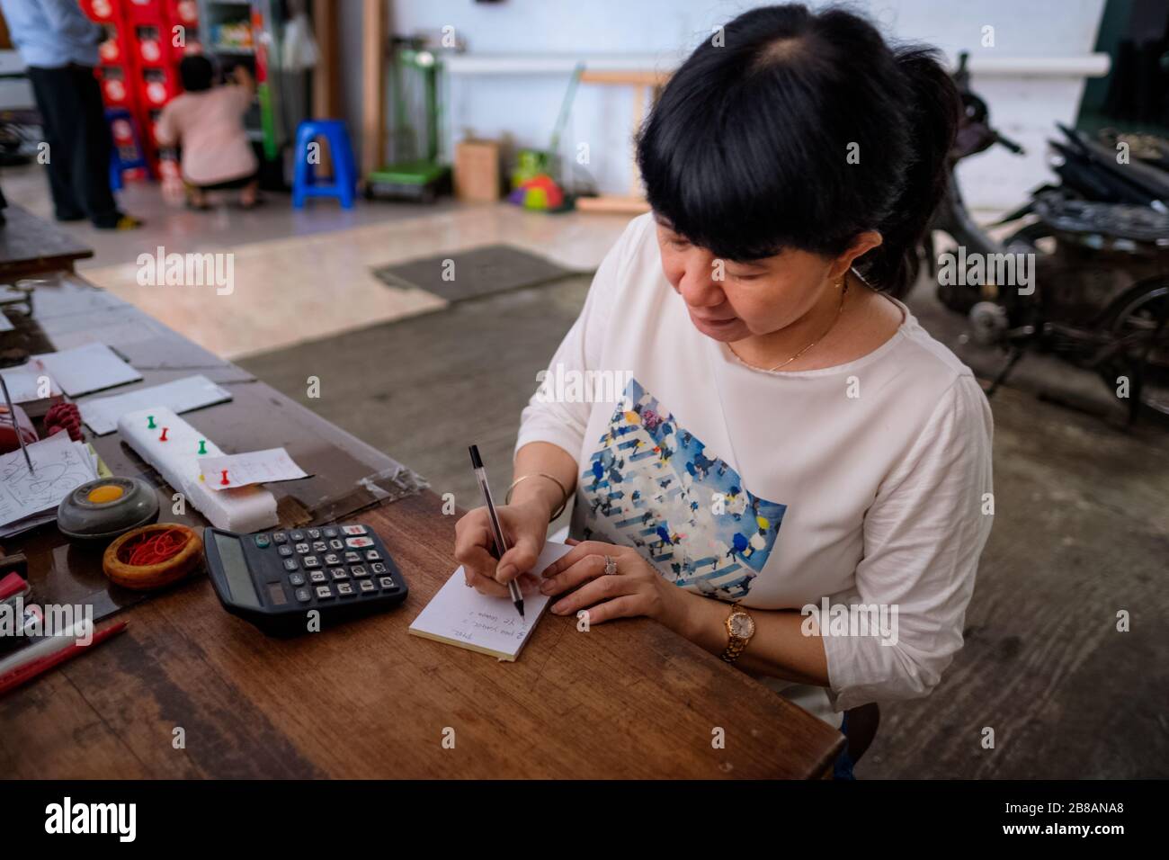 Le donne indonesiane asiatiche, il proprietario del piccolo deposito locale di affari della famiglia-proprietà, o localmente denominato warung, calcolando il profitto dalla sua scrivania. Focu. Selettivo Foto Stock