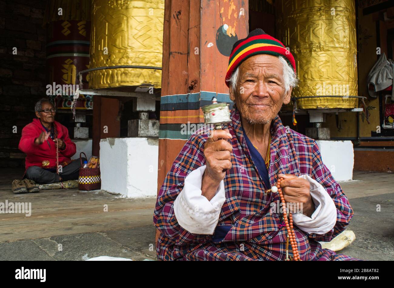 Il vecchio bhutanese che gode il suo pensionamento in un monastero e che pratica la preghiera buddista a Thimphu, Bhutan in abito tradizionale Foto Stock