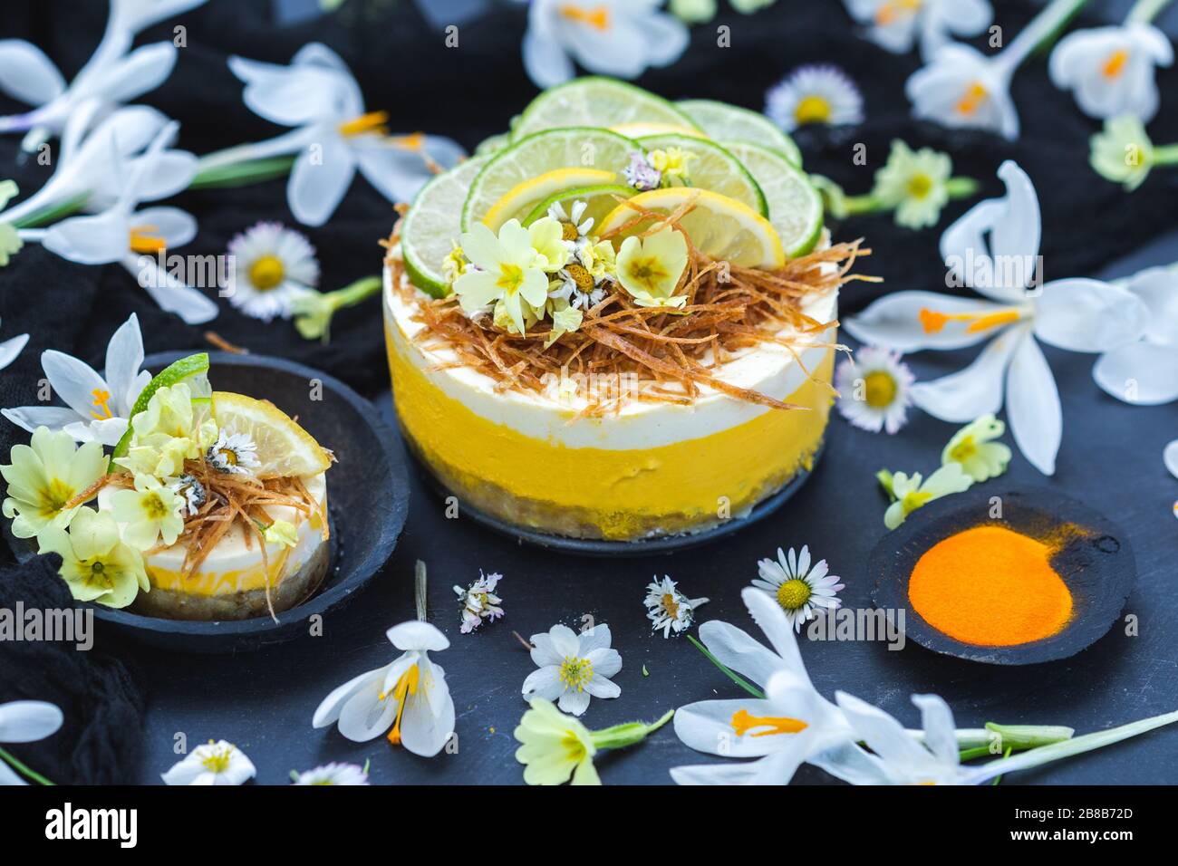 Torta vegana cruda con limone e lime su un nero superficie ricoperta da minuscoli fiori a margherita Foto Stock