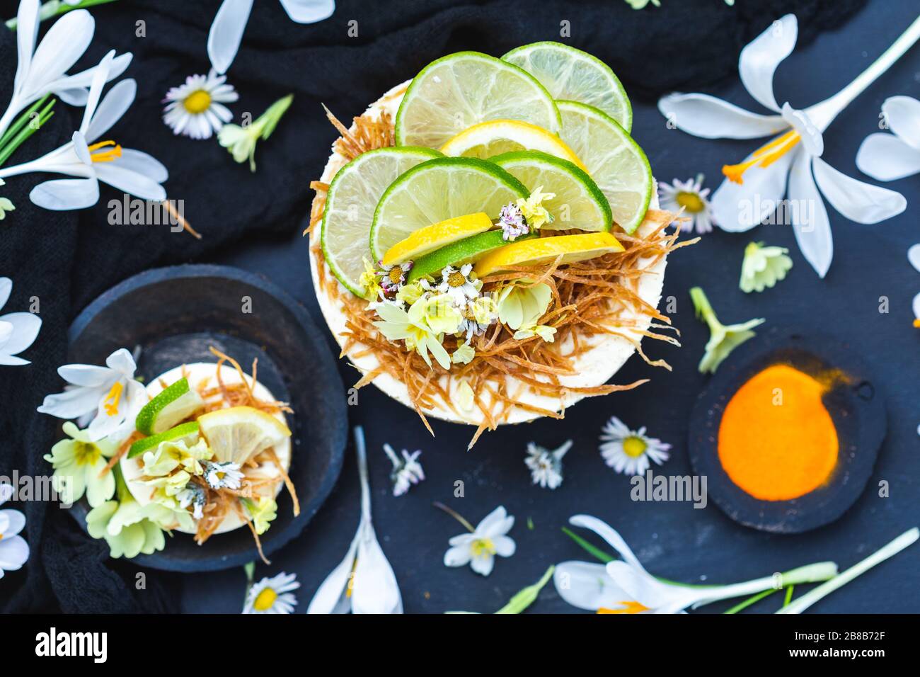 Torta vegana cruda con limone e lime su un nero superficie ricoperta da minuscoli fiori a margherita Foto Stock