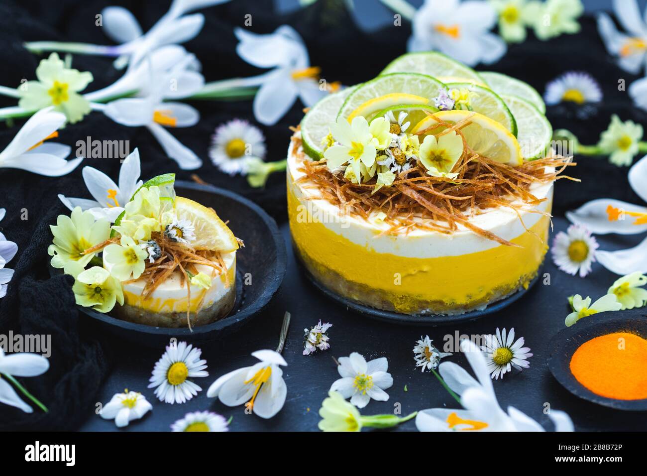 Torta vegana cruda con limone e lime su un nero superficie ricoperta da minuscoli fiori a margherita Foto Stock