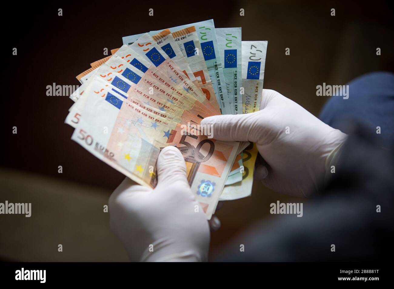 Uomo in possesso di banconote in euro con le mani che indossano guanti chirurgici per proteggere da batteri e virus. Foto Stock