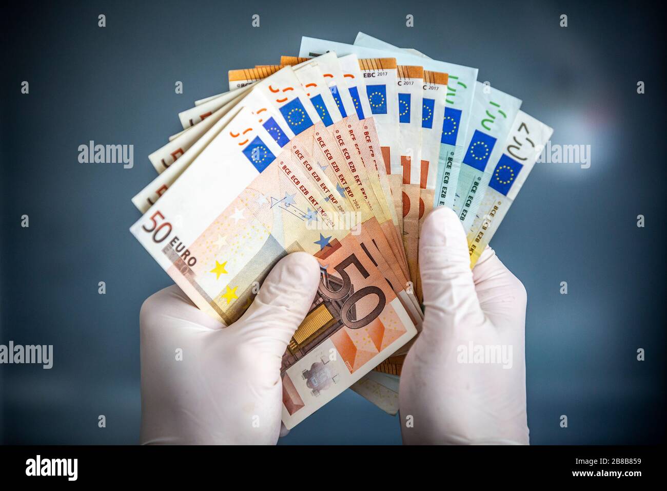 Uomo in possesso di banconote in euro con le mani che indossano guanti chirurgici per proteggere da batteri e virus. Foto Stock