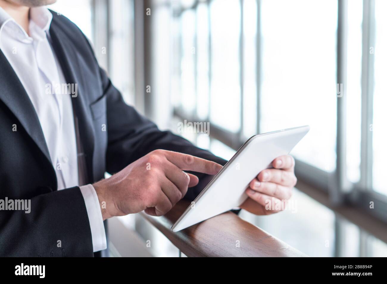 Uomo d'affari che usa il tablet vicino alla finestra in un moderno edificio di vetro per uffici. Uomo d'affari che ha un dispositivo mobile intelligente e che lavora. Premere il touch screen. Foto Stock