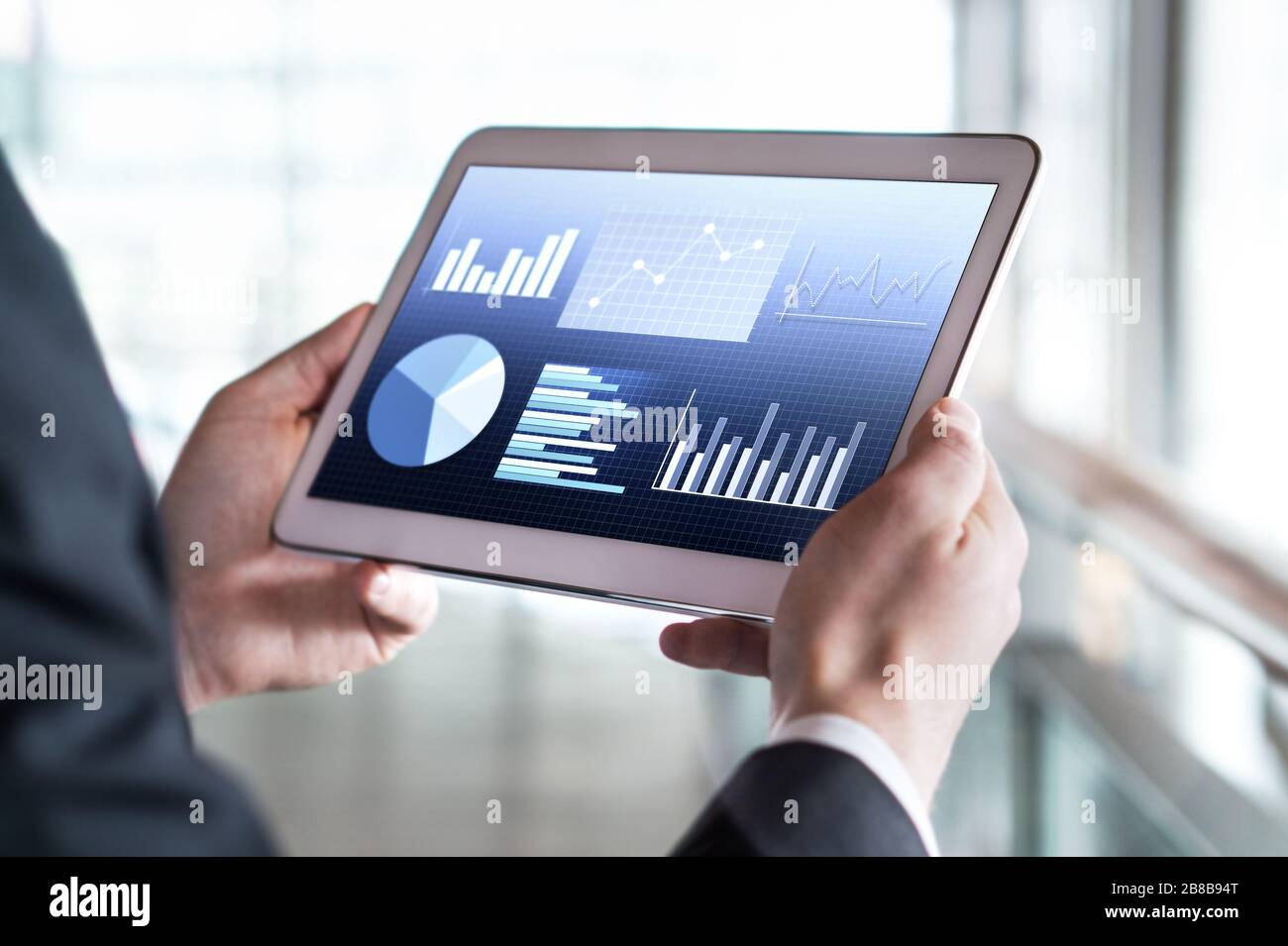 Primo piano di un uomo d'affari che usa un tablet in un moderno edificio d'ufficio. Uomo che legge le statistiche finanziarie, i grafici di affari ed i dati commerciali. Foto Stock