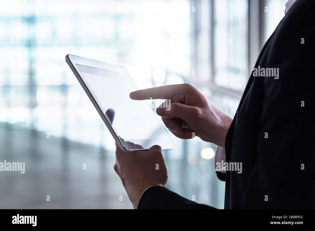 Uomo in tuta con tablet. Uomo d'affari con dispositivo mobile intelligente in un moderno edificio in vetro. Foto Stock