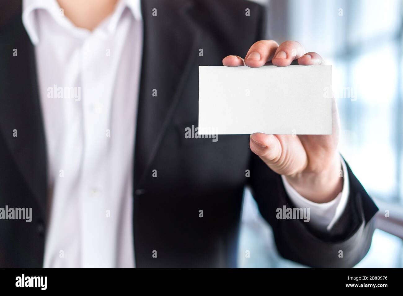 Uomo d'affari professionale che tiene un biglietto da visita bianco vuoto in un moderno edificio d'ufficio. Spazio libero per la copia. Foto Stock