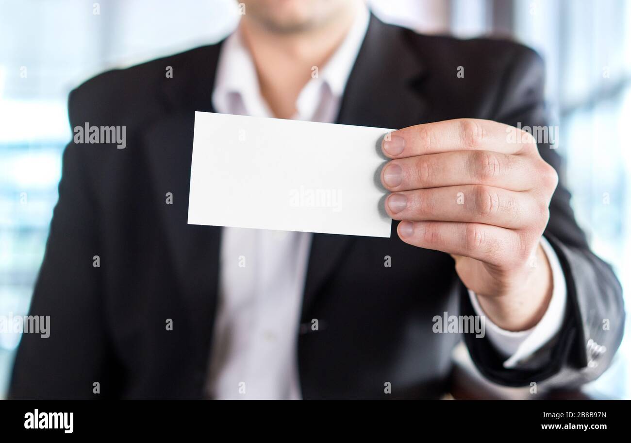 Uomo d'affari in possesso di un biglietto da visita bianco vuoto in un moderno edificio d'ufficio. Spazio libero per la copia. Foto Stock