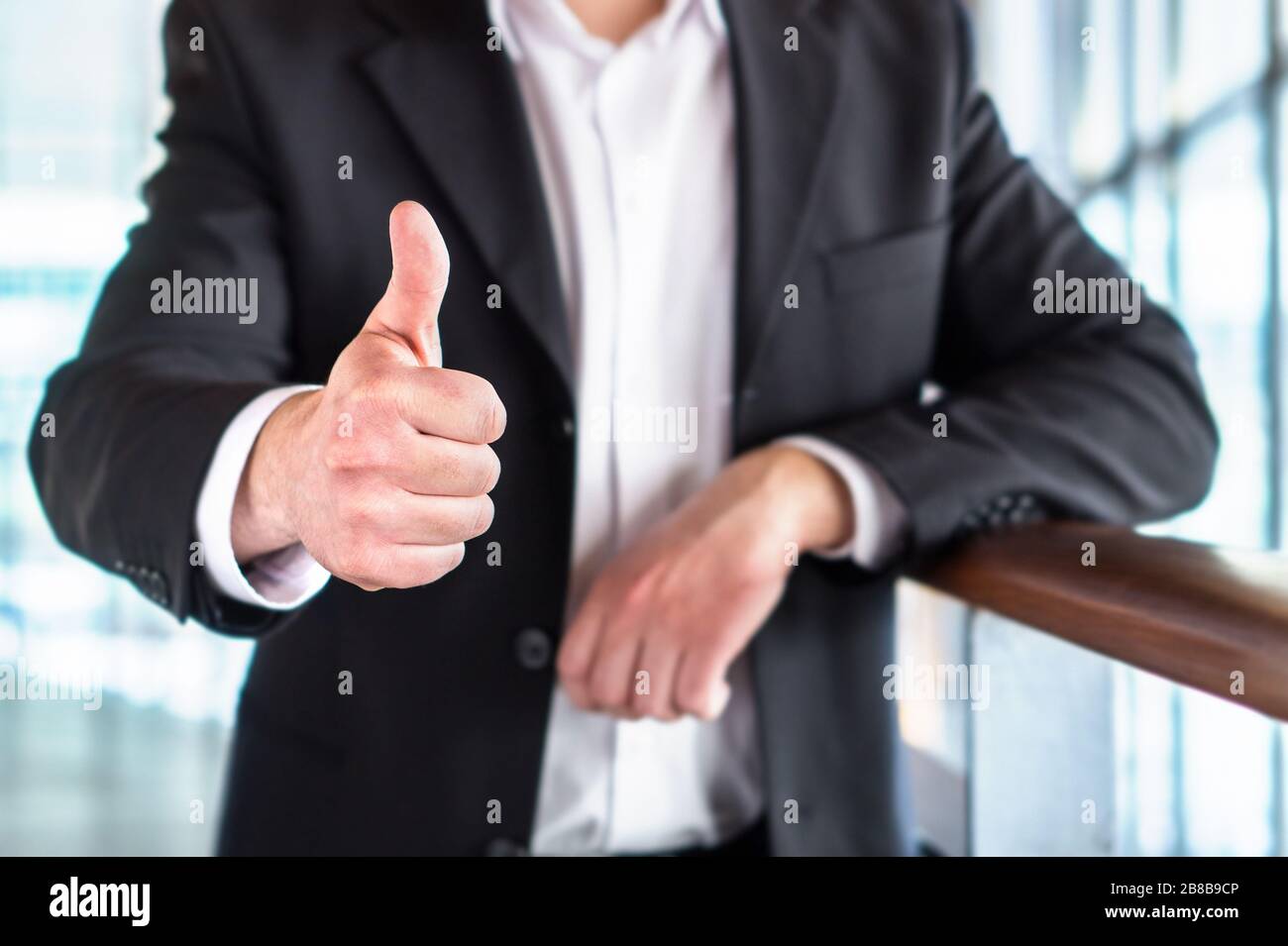 Uomo d'affari o avvocato che dà i pollici in su nell'edificio moderno dell'ufficio. Buon uomo d'affari che mostra un gesto di mano soddisfatto e di supporto. Foto Stock