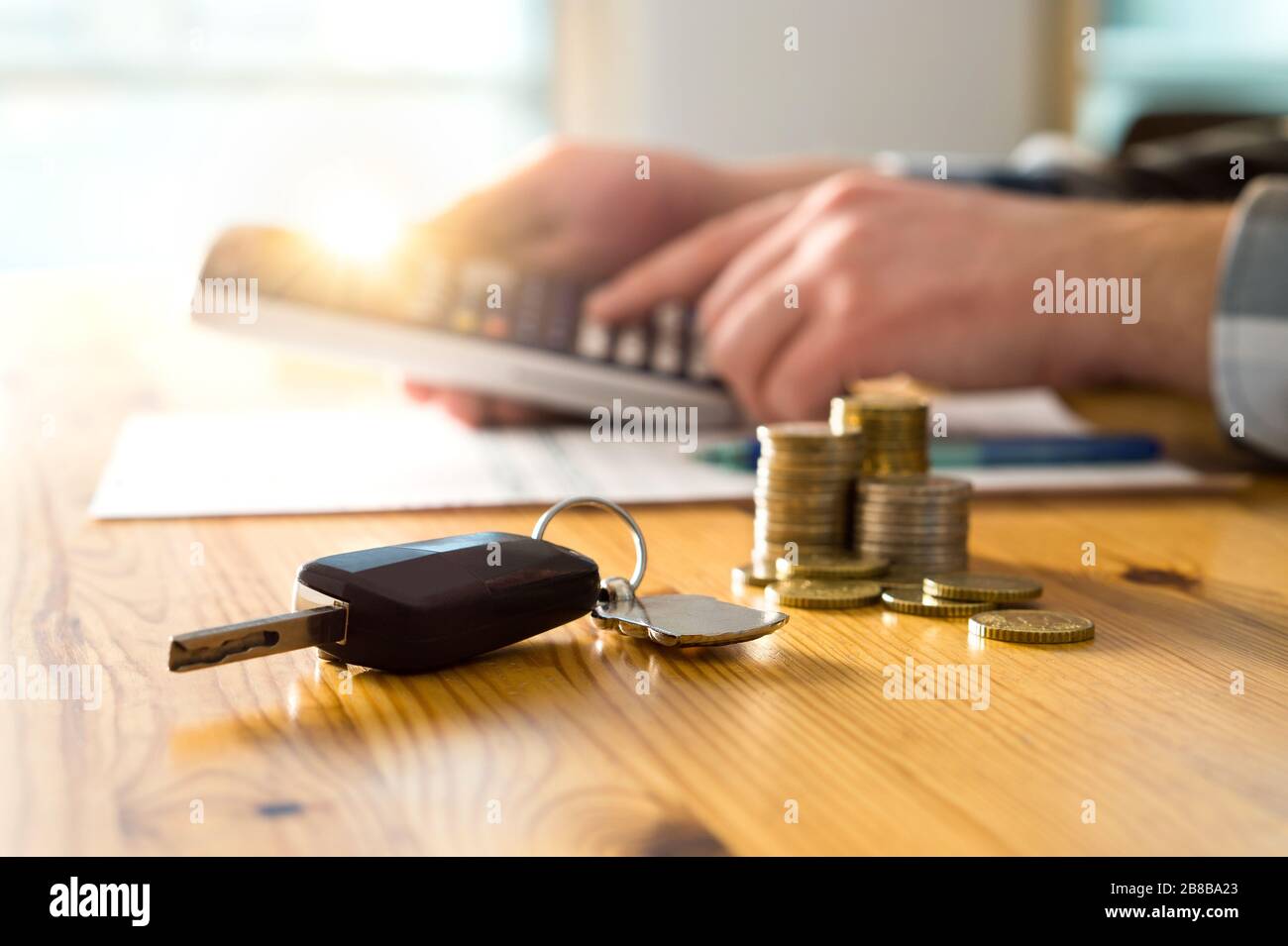 Chiavi auto e denaro sul tavolo con l'uomo che usa la calcolatrice. Compratore che conta i risparmi ed il costo del gas o venditore che calcola il prezzo di vendite. Foto Stock