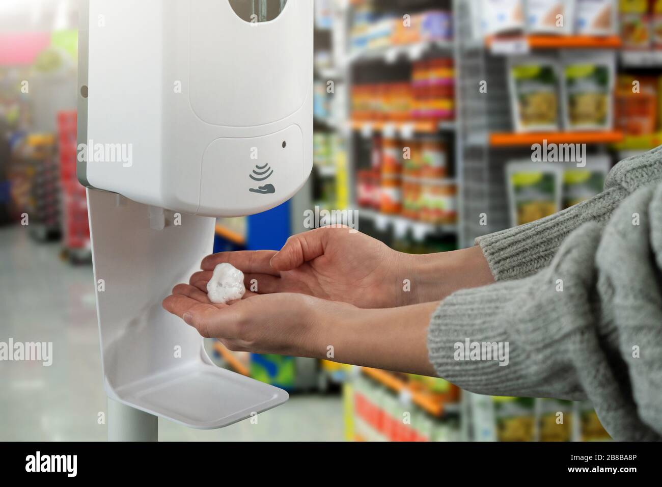 Donna tratta le mani con un disinfettante in un negozio di alimenti durante l'epidemia di coronavirus Foto Stock
