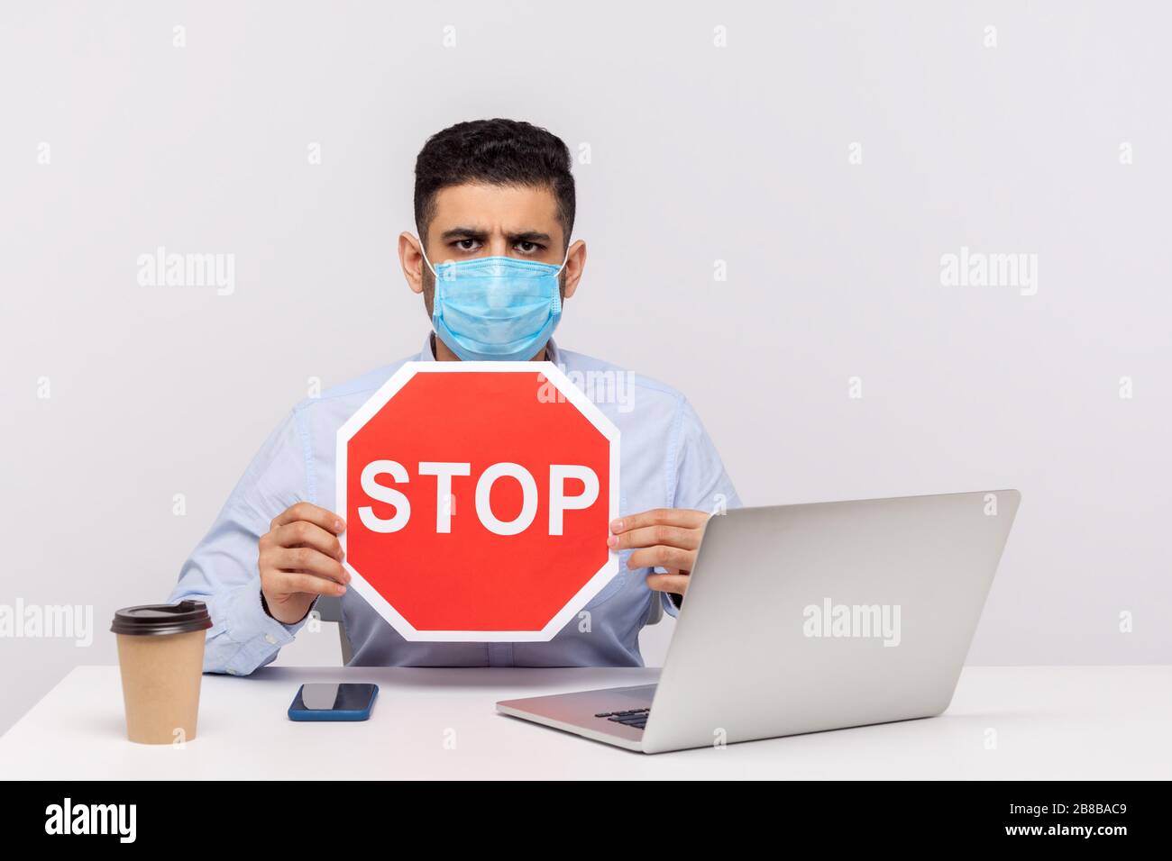 Lavoratore in ufficio in maschera igienica tenuta rossa Stop segno di avvertimento di contagiosa epidemia di coronavirus, quarantena e misure preventive per la diffusione di infe Foto Stock