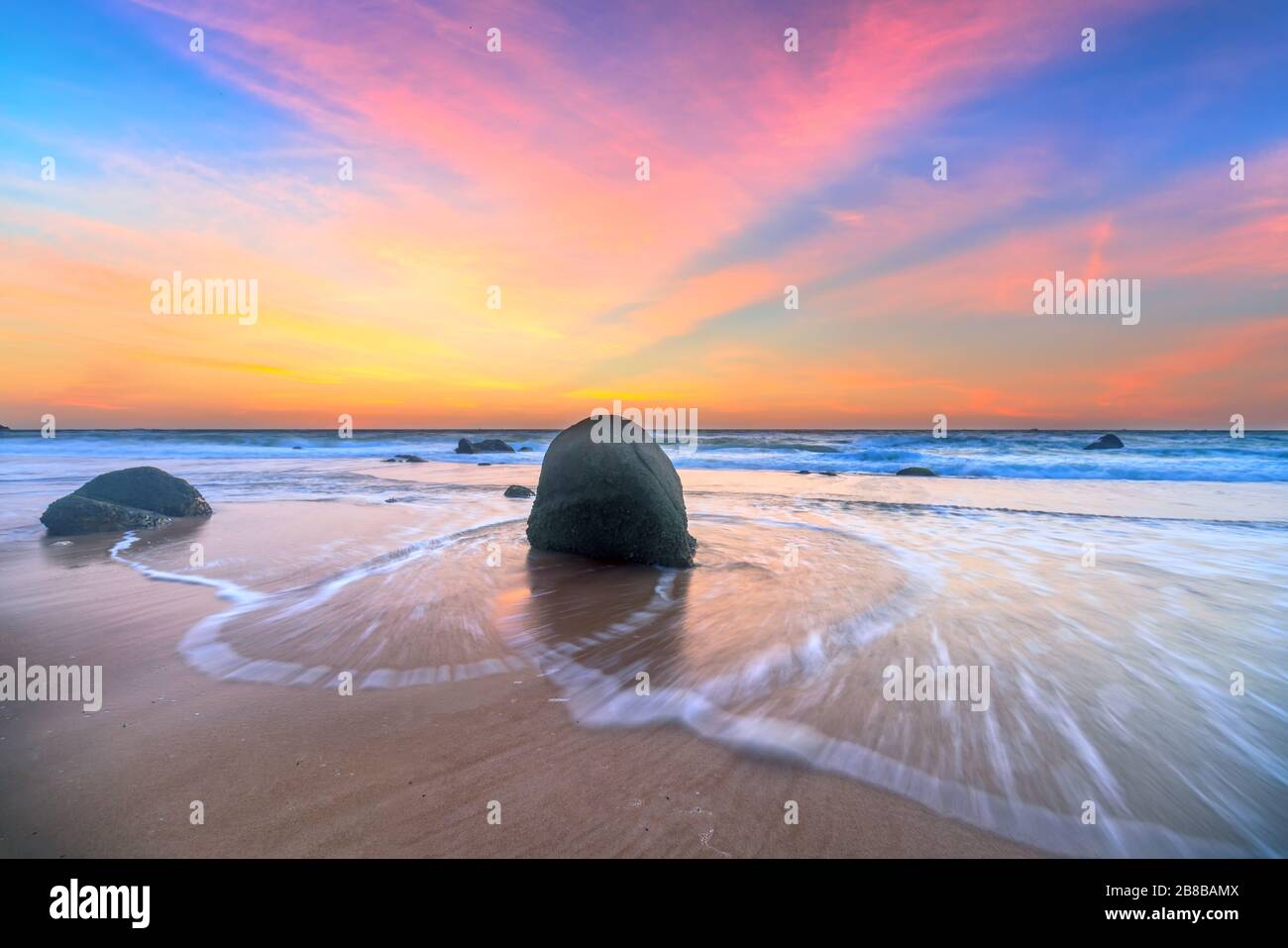 Dawn su una bellissima bache con onde che si infrangono sulla riva creando striature serigrafiche di forme diverse che perforano la roccia. Foto Stock