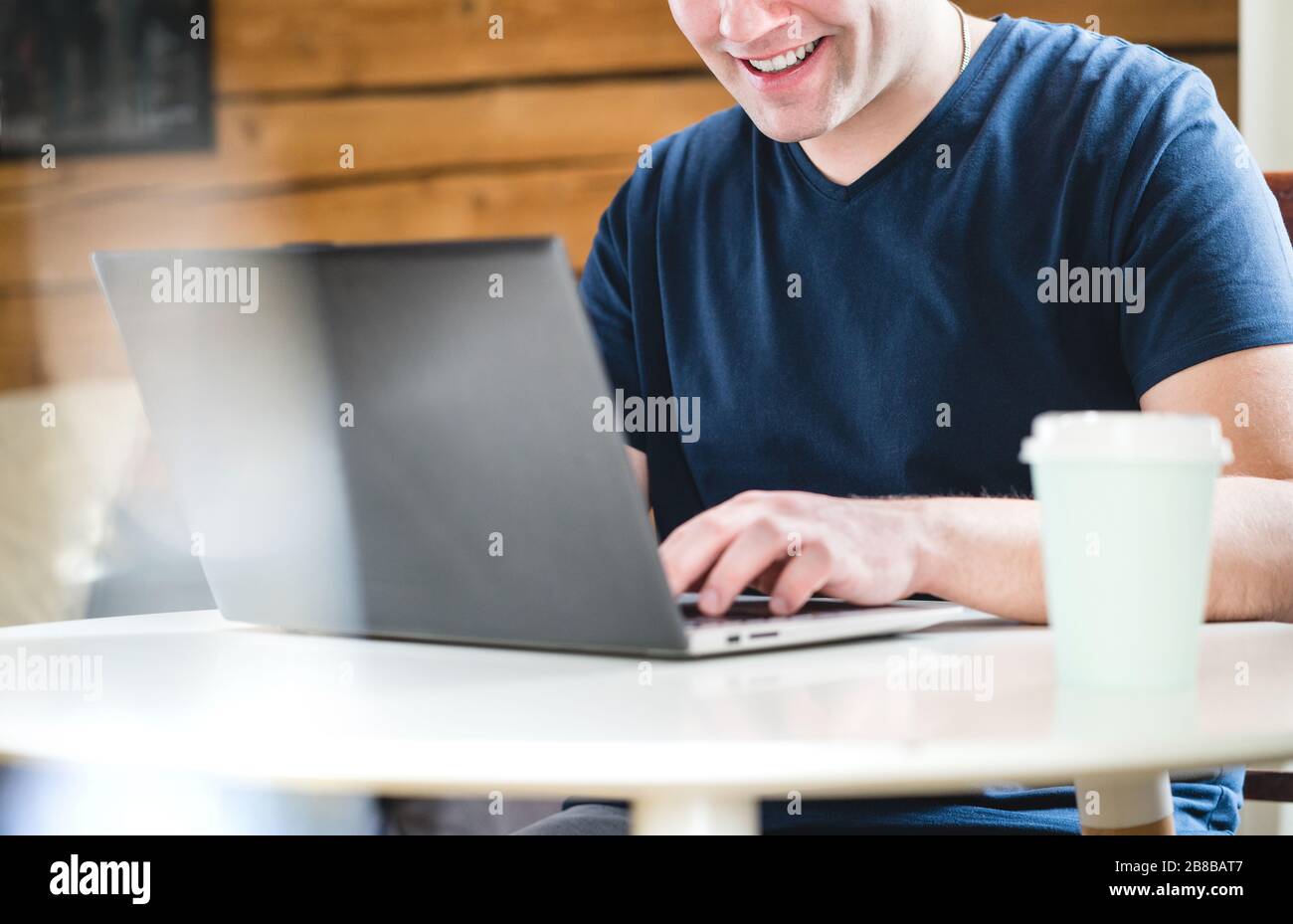 Buon uomo che usa un computer portatile o un bar. Sorridente con il computer e take via la tazza di caffè sul tavolo. Foto Stock