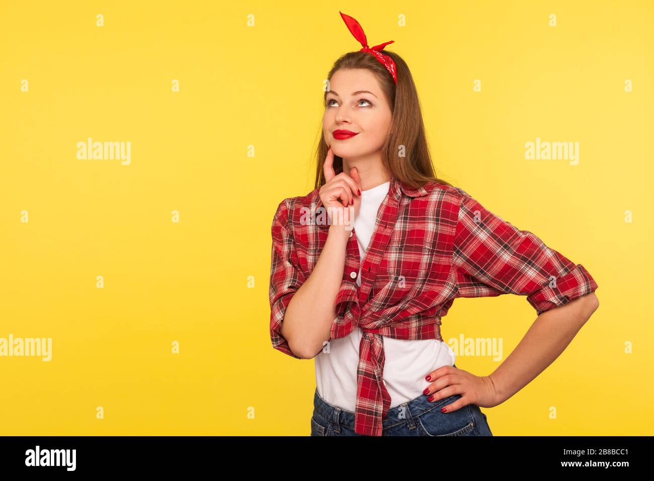 Ritratto di attraente PINUP PINSINSive ragazza in camicia a scacchi e fascia in piedi pensieroso, prendere la decisione, contemplando con confusa e dubbia Foto Stock