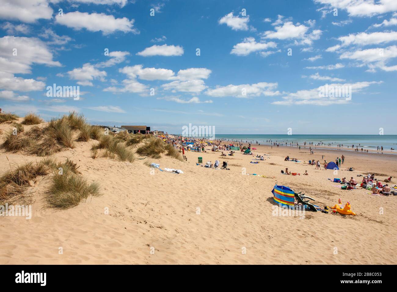 Gruppi di persone che si rilassano e godono di una bella calda giornata di sole alla spiaggia di Camber Sands Foto Stock