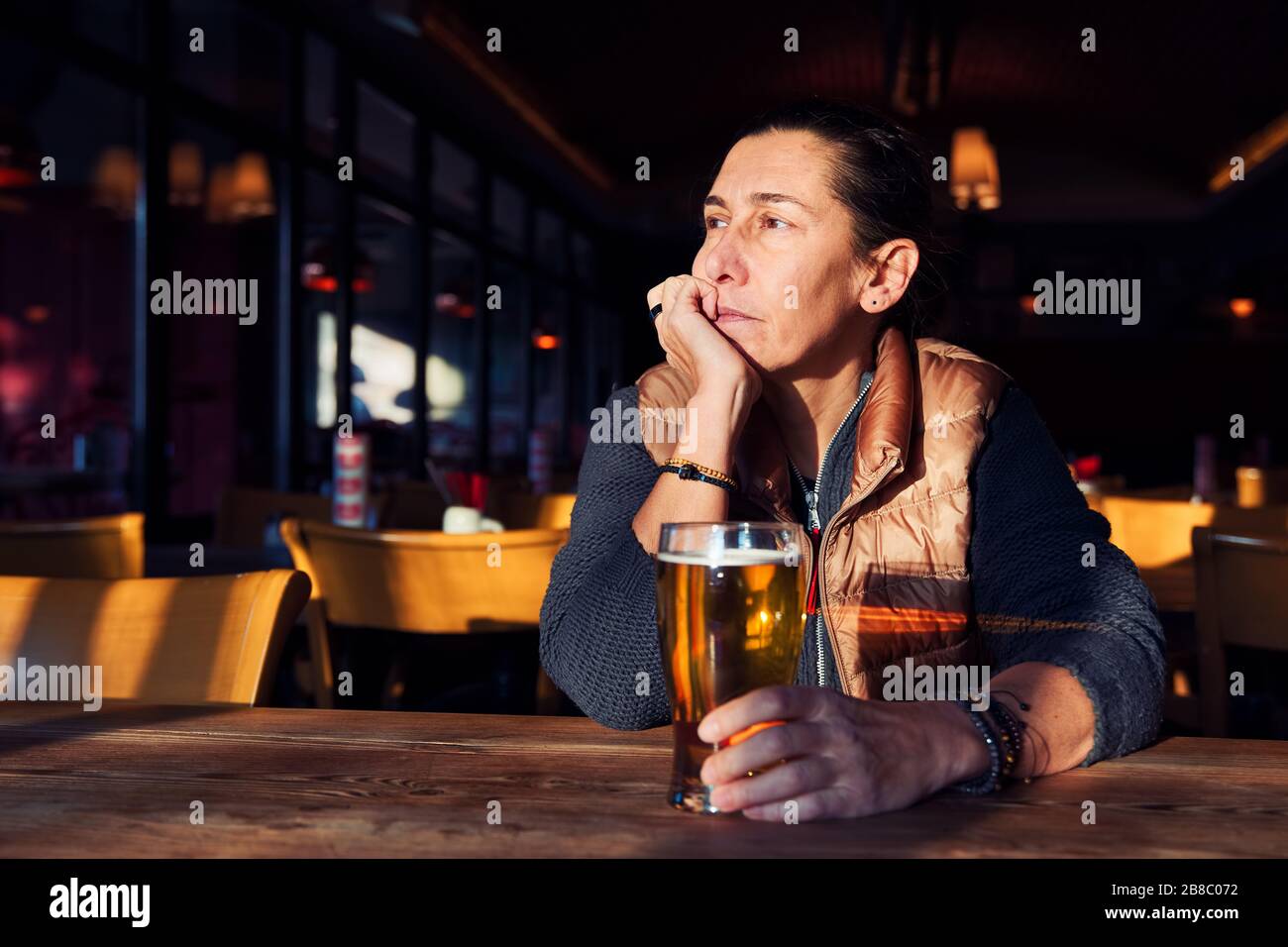 Una donna malcontenta, depressa e solitaria di mezza età seduta al bar con un bicchiere di birra. Foto Stock