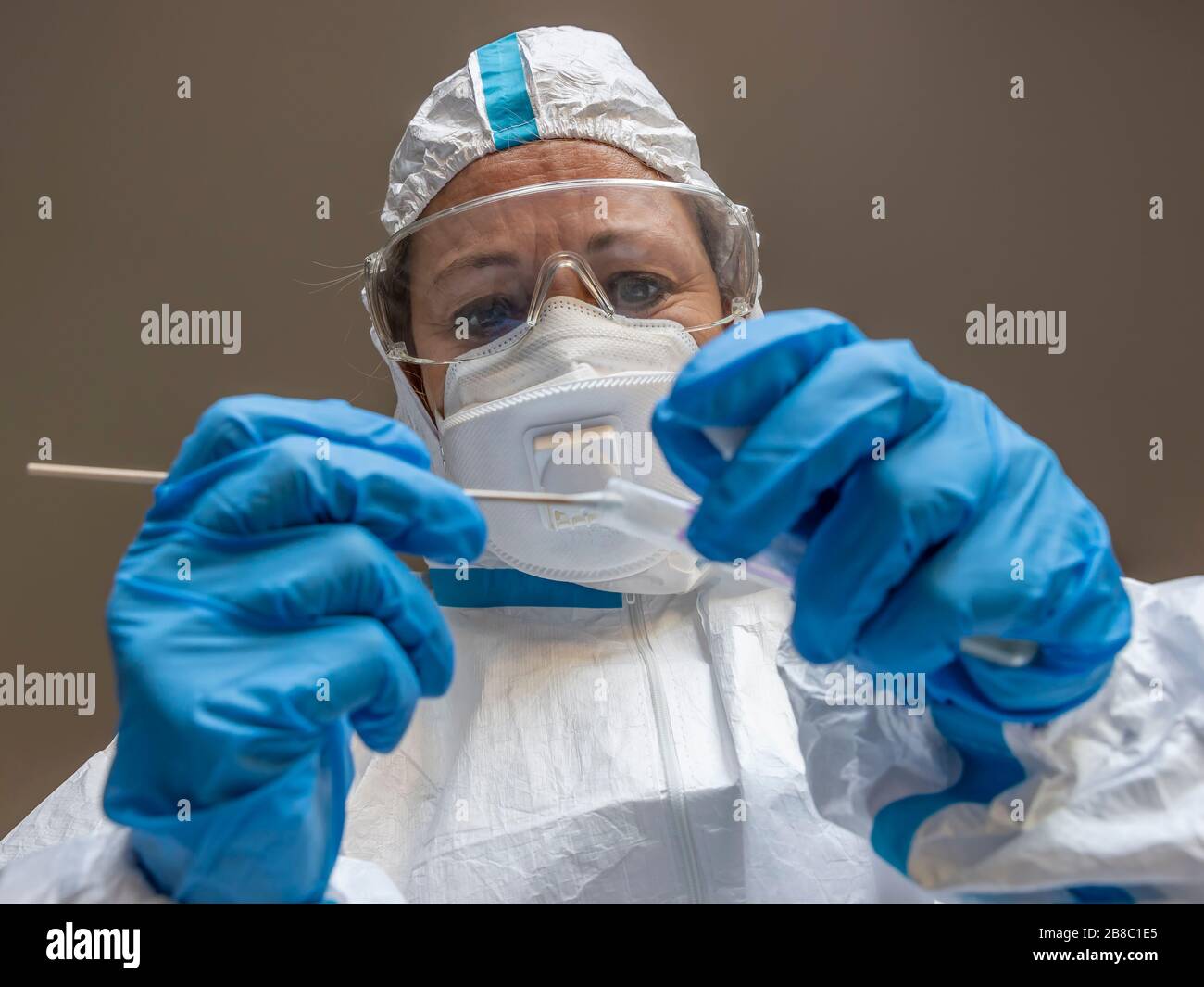 Una donna, un tecnico di laboratorio, coperta da una tuta bianca protettiva, effettua un tampone di prova per verificare la presenza di un possibile contagio da Coronavirus Covid-19 Foto Stock