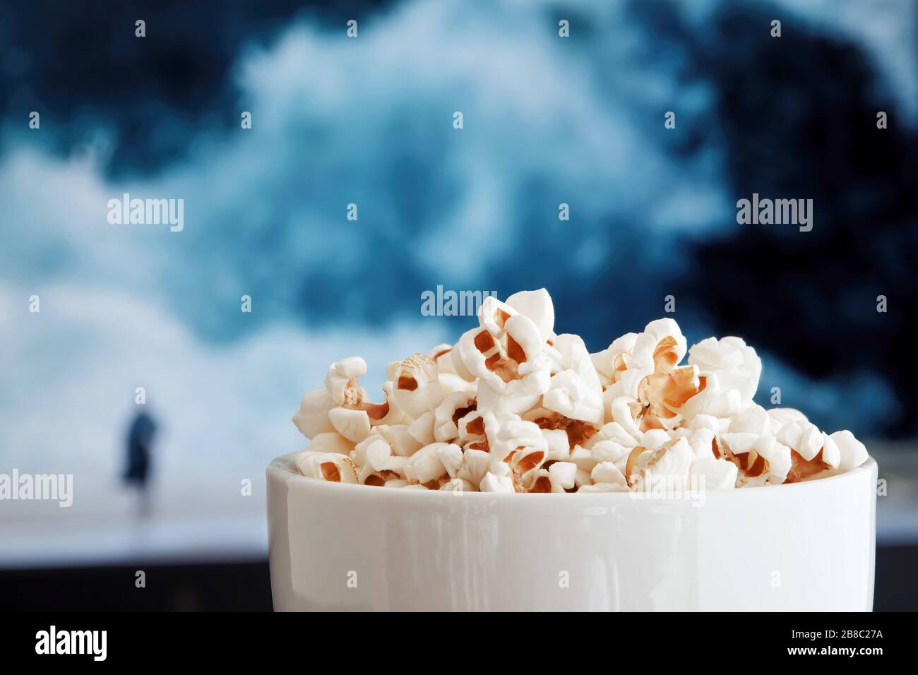 Ciotola piena di popcorn contro lo schermo della tv con i film riprodotti sopra. Foto Stock