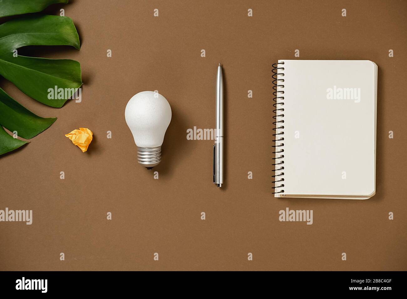 Idee ispirazione concetti con lampadina, penna, foglie di mostera, occhiali, notebook con spazio copia su sfondo carta marrone stile minimal. Templat Foto Stock
