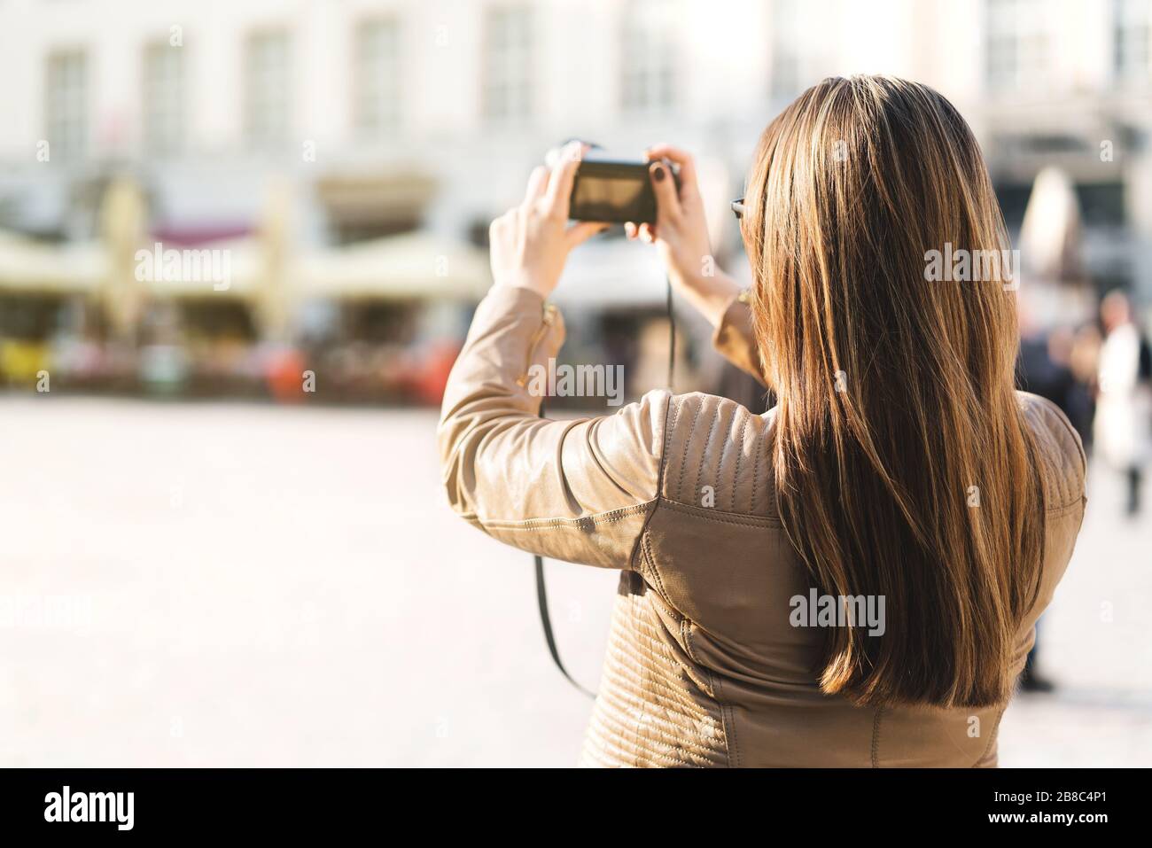 Turista scattare foto della piazza della città durante le vacanze con la macchina fotografica. Donna che fotografa la vacanza in città. Concetto di turismo. Vista posteriore della persona femminile. Foto Stock