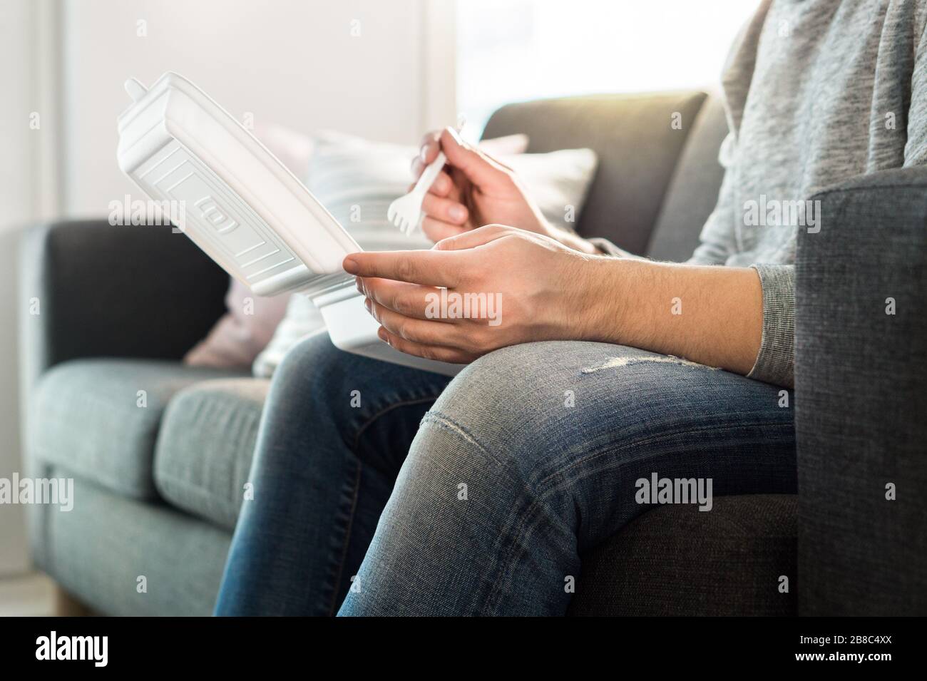 Buon uomo che mangia fast food da portare a casa scatola sul divano. Guy gustando kebab o insalata. Cena take-out dal ristorante cinese o junk food. Foto Stock