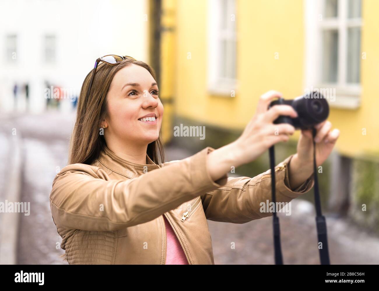 Felice donna che scatta foto con la fotocamera. Turista in vacanza in strada della città. Foto delle vacanze. Sorridente fotografo o hobbista. Foto Stock