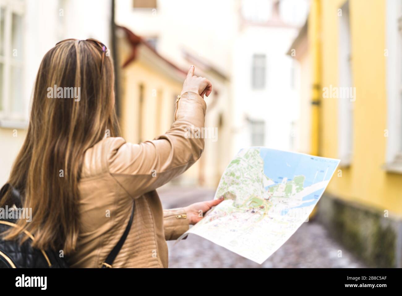 Turistico con mappa in città. Donna che punta verso destra con il dito. Vista posteriore del viaggiatore felice usando la guida turistica. Persona con zaino. Foto Stock