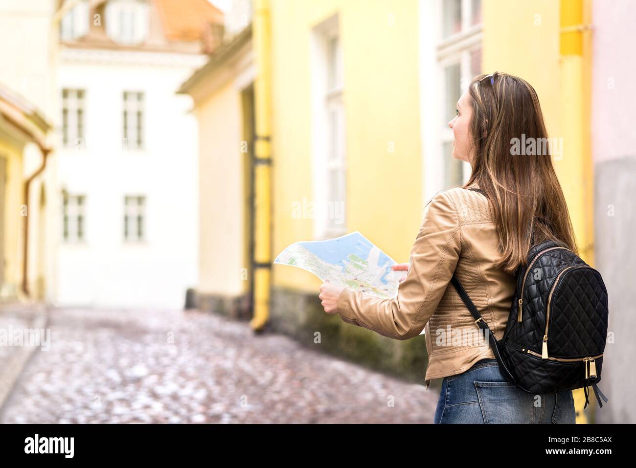 Donna a piedi e tenendo mappa nella strada della città. Vista posteriore del turista femminile e del viaggiatore con zaino di ricerca destinazione durante la vacanza. Foto Stock