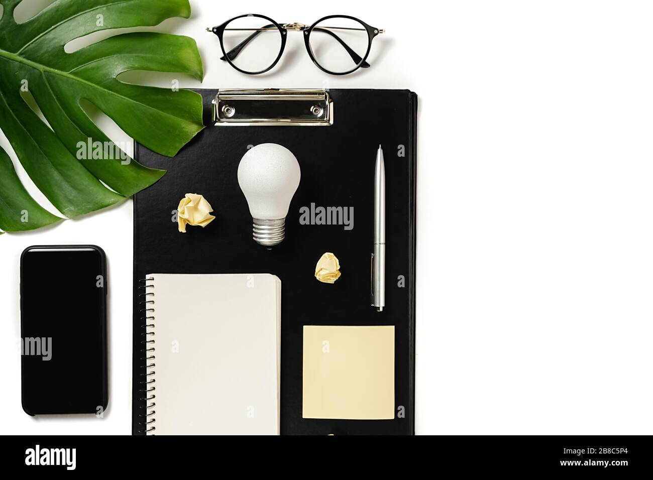 Piano tavolo di pianificazione finanziaria con appunti mockup, foglie di mostera, penna, notebook, smartphone moderno, occhiali e lampadina su sfondo bianco m Foto Stock
