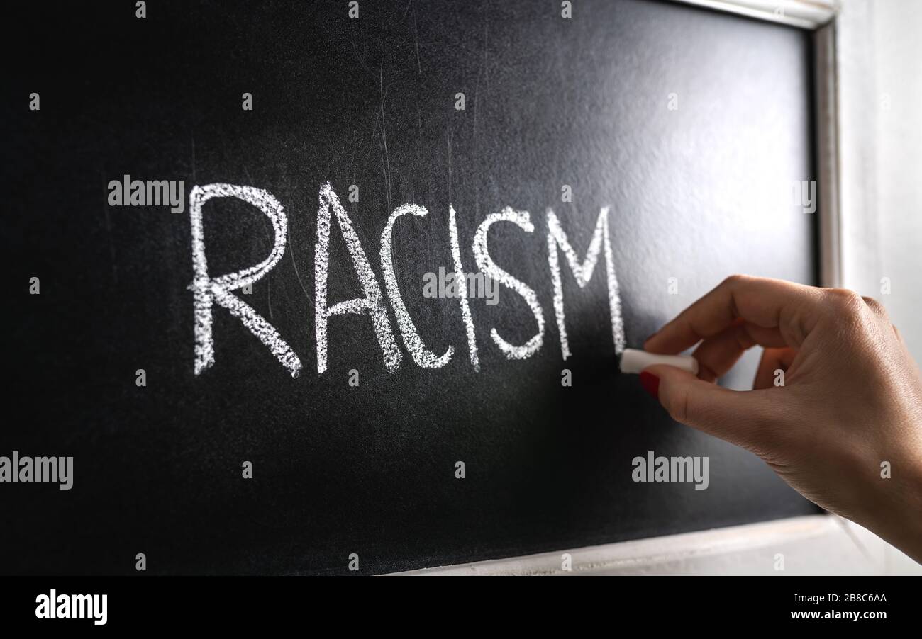 Mano che scrive la parola razzismo sulla lavagna. Stop all'odio. Contro il pregiudizio e la violenza. Conferenza sulla discriminazione o gli stereotipi a scuola. Foto Stock