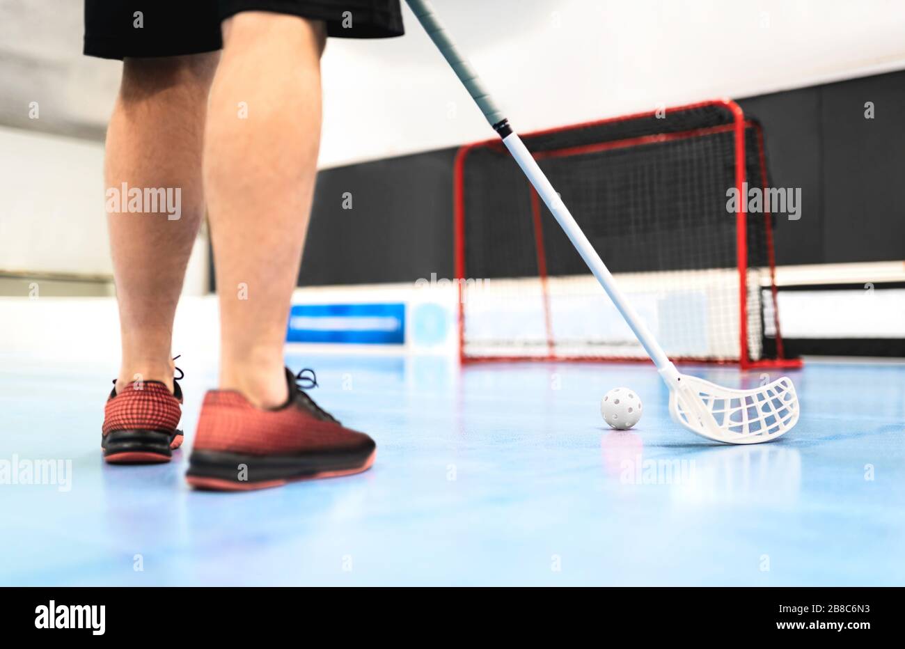 Vista posteriore dell'addestramento del giocatore del floorball con bastone, palla e gol sul campo. Uomo che gioca nell'arena dell'hockey del pavimento. Foto Stock