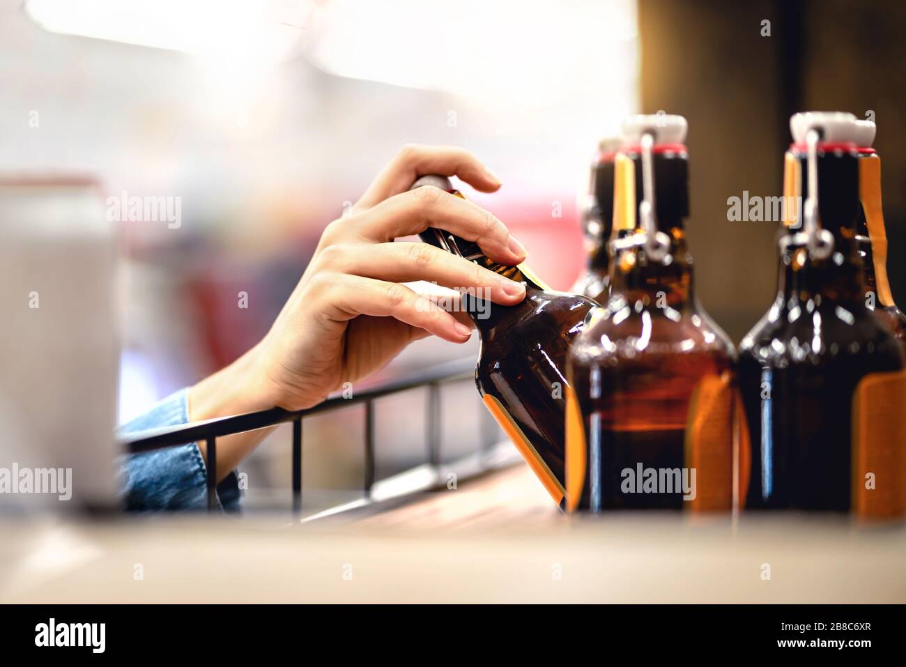 Consegna a mano una bottiglia di birra dallo scaffale in un negozio di alcolici e liquori. Cliente che acquista sidro o supermercato personale riempire e stoccaggio scaffali. Foto Stock