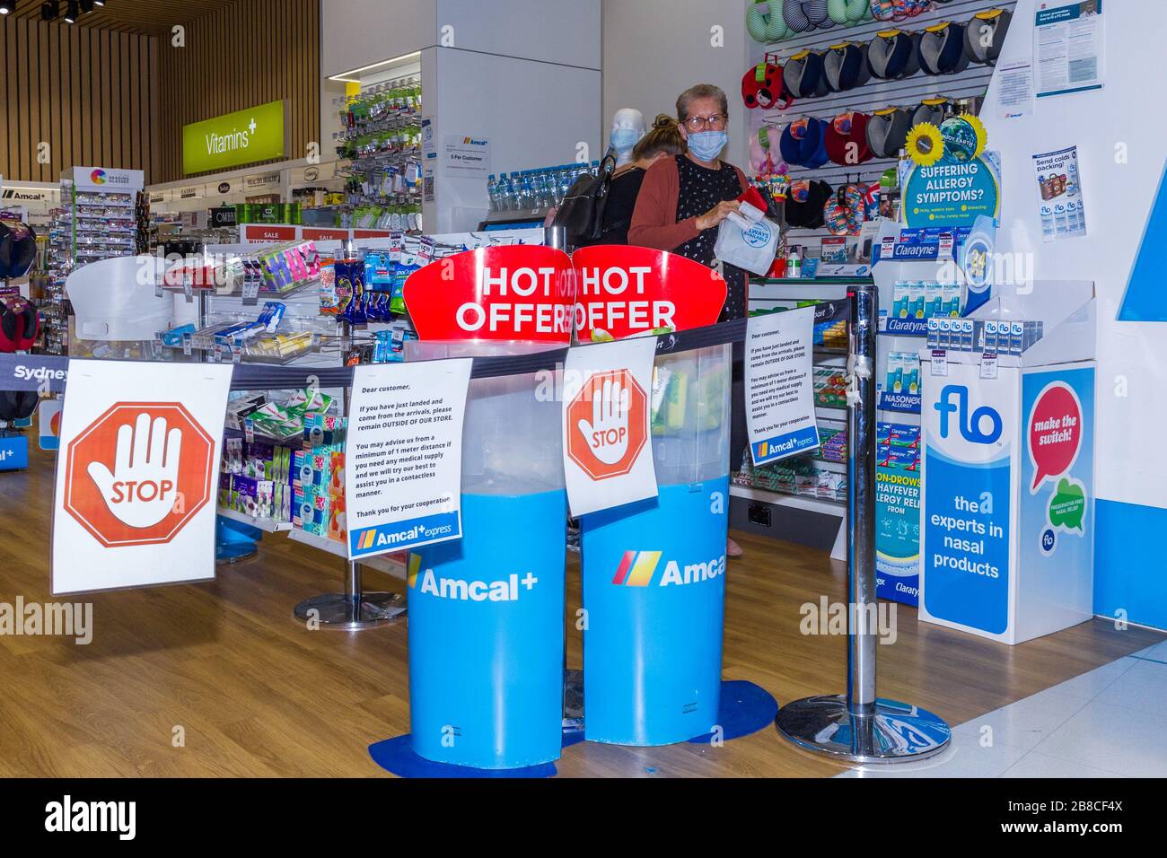 Segnali di allarme per coronavirus e barriere di sicurezza presso una farmacia Amcal presso il terminal delle partenze internazionali dell'aeroporto di Sydney (Kingsford Smith) in Australia. Il chimico aveva posto la barriera e gli avvertimenti all'ingresso del negozio per chiedere ai passeggeri della compagnia aerea appena arrivati in Australia di aderire alle regole di "allontanamento sociale" per ridurre il rischio di diffusione del Coronavirus. Foto Stock