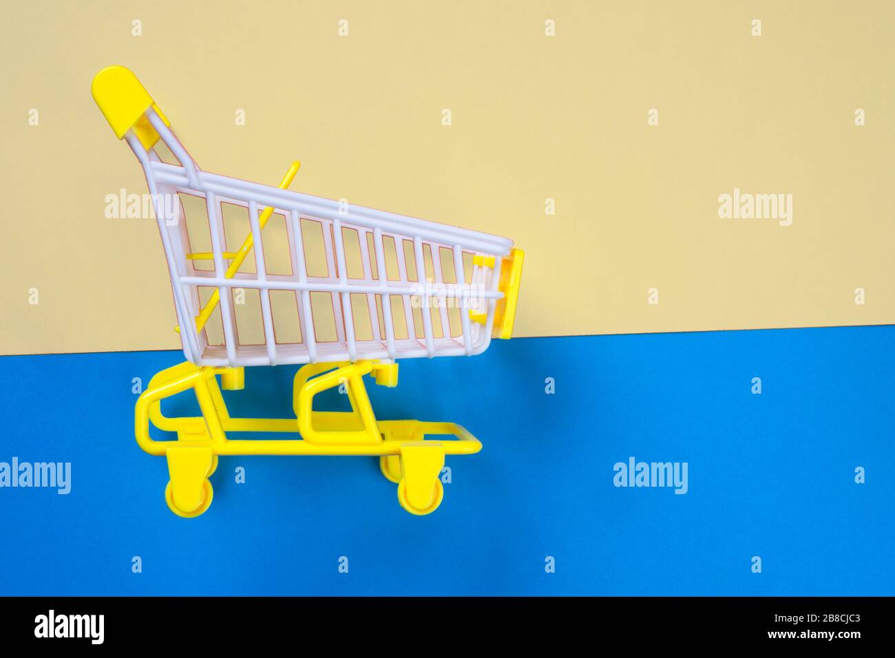 Carrello piccolo shopping su sfondo giallo e blu, spazio copia. Vendita o acquisto di concetto di consumatore Foto Stock