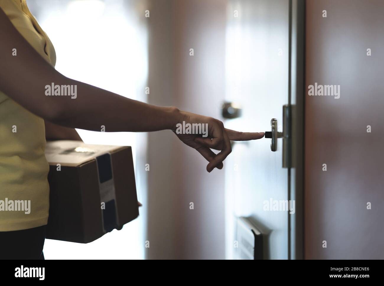 La persona di consegna squilla il campanello mentre consegna il pacchetto alla porta di casa. Corriere che porta la scatola ordinata al cliente. Concetto di spedizione. Foto Stock