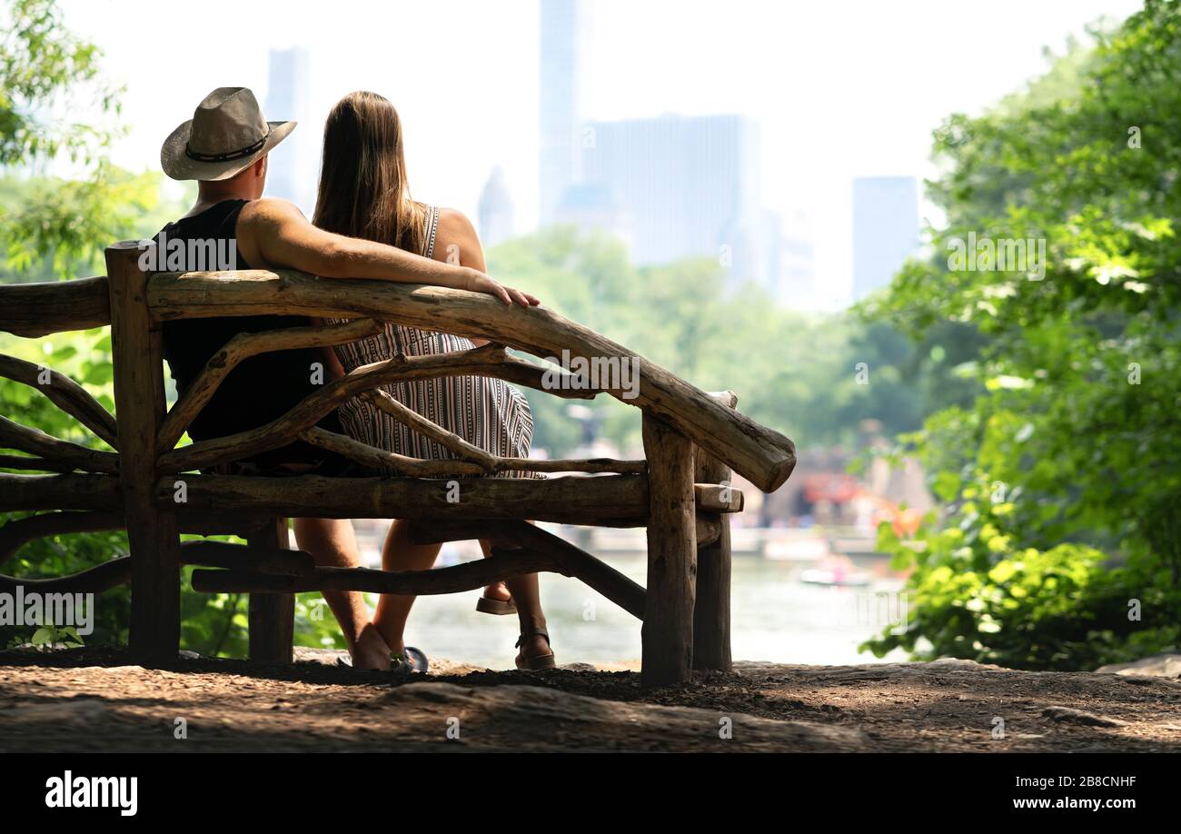 Coppia seduta su una panchina del parco e con un romantico primo appuntamento. Amanti del romanticismo e della fiducia. Vista sul retro di un uomo e una donna felici che guardano l'edificio. Foto Stock