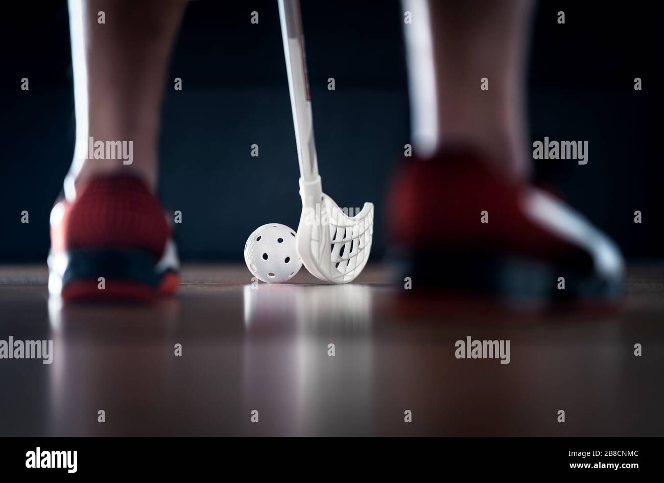 Giocatore di Floorball in piedi con bastone e palla su. Hockey da pavimento. Vista posteriore tra le sneakers. Luce drammatica. Foto Stock