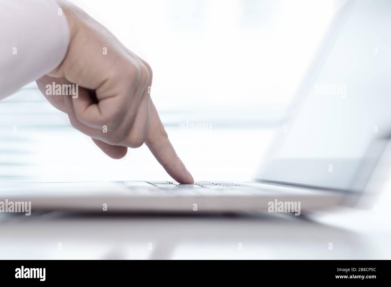 Un unico dito che preme il pulsante della tastiera nel computer portatile con sfondo sfocato. Un uomo indica i tasti con mano, la digitazione o toccando il computer. Foto Stock