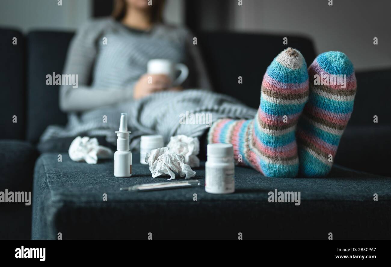 Donna malata che riposa sul divano tenendo una tazza di tè caldo. Persona malata con influenza, freddo, febbre o virus seduto sul divano a casa in inverno. Medicina, termometro. Foto Stock