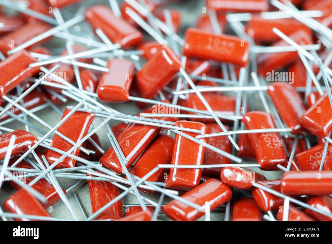 Il primo piano di un gruppo di condensatori rossi si trova l'uno sopra l'altro in una fabbrica di computer e apparecchiature per ufficio. Concetto di parti di qualità. Lotto all'ingrosso Foto Stock