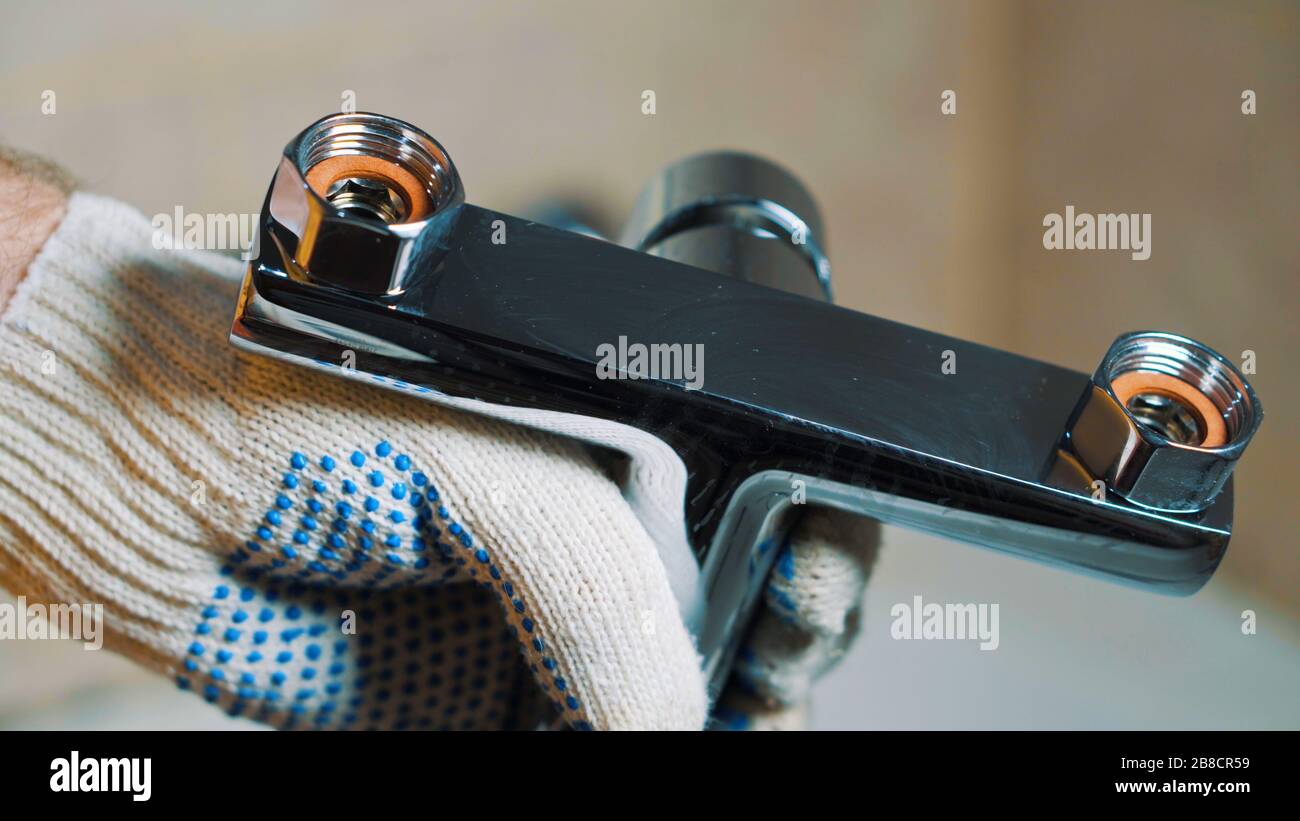 Primo piano di un idraulico con guanti che tiene un rubinetto dell'acqua. Lo installerà. Foto Stock