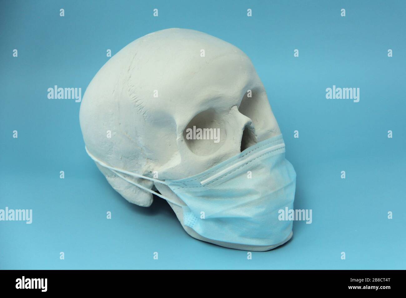 Cranio umano bianco in gesso con maschera medica su sfondo blu. Il concetto di pandemia, medicina e coronovirus. Foto Stock